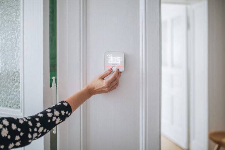Eine Hand bedient ein Bosch Raumthermostat an einer Wand