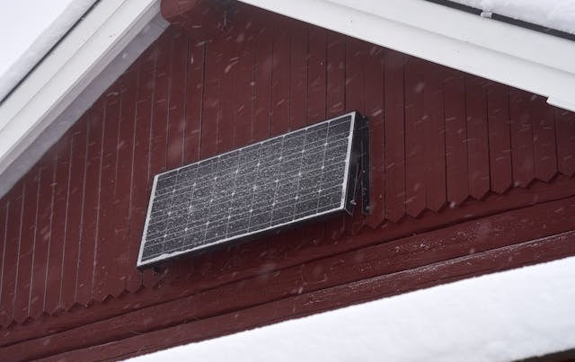 Senkrecht  montiertes  Solarmodul  an  einer  roten  Hauswand  bei  Schneefall