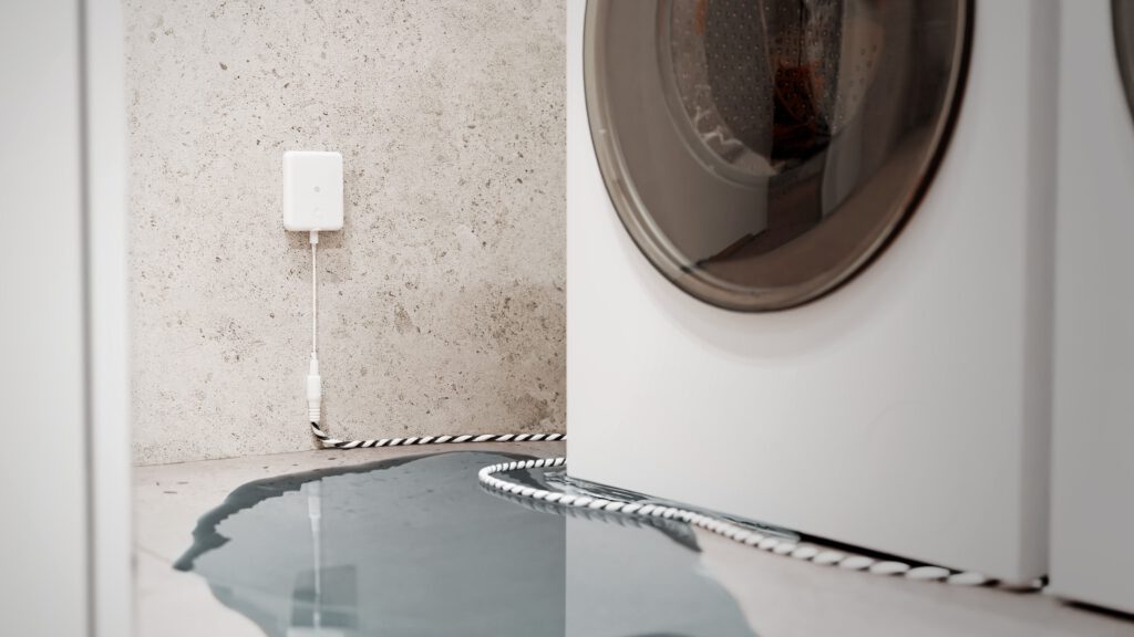 Herstellermotiv: Shelly Flood Gen4 an der Wand neben einer Waschmaschine, Sensorkabel und Wasser auf dem Boden